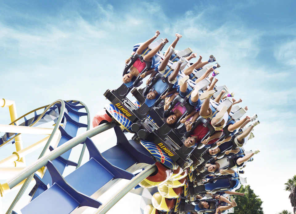 People on a roller coaster are upside down during a loop, with blue track and a clear sky visible in the background.