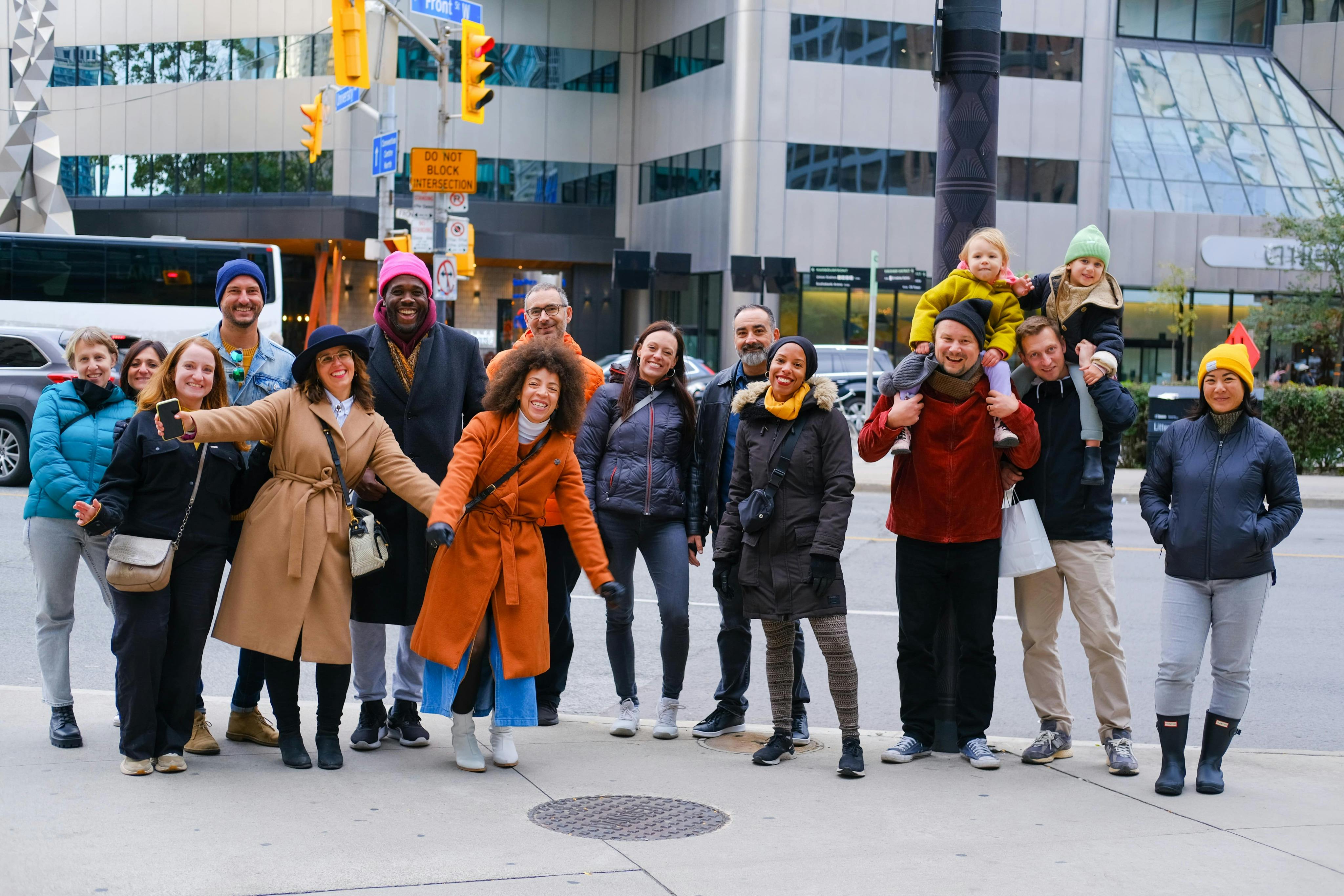 一群人在城市人行道上微笑着摆姿势，背景是建筑物和交通标志。