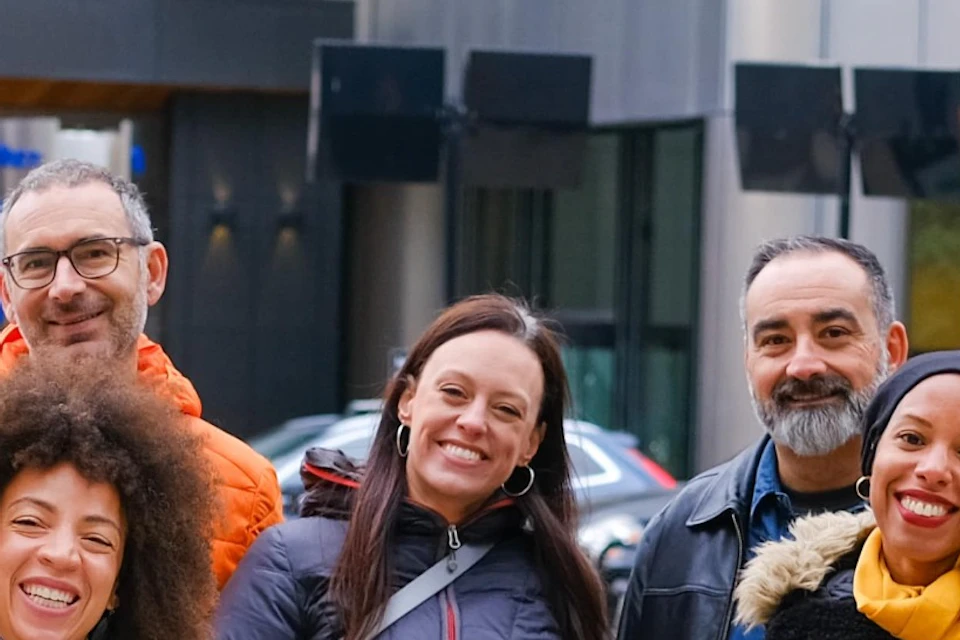 A group of people smiling and posing together on a city sidewalk with buildings and traffic signs in the background.