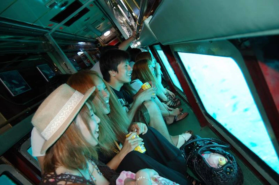 A group of people sitting inside a vehicle with large glass windows displaying an underwater view.