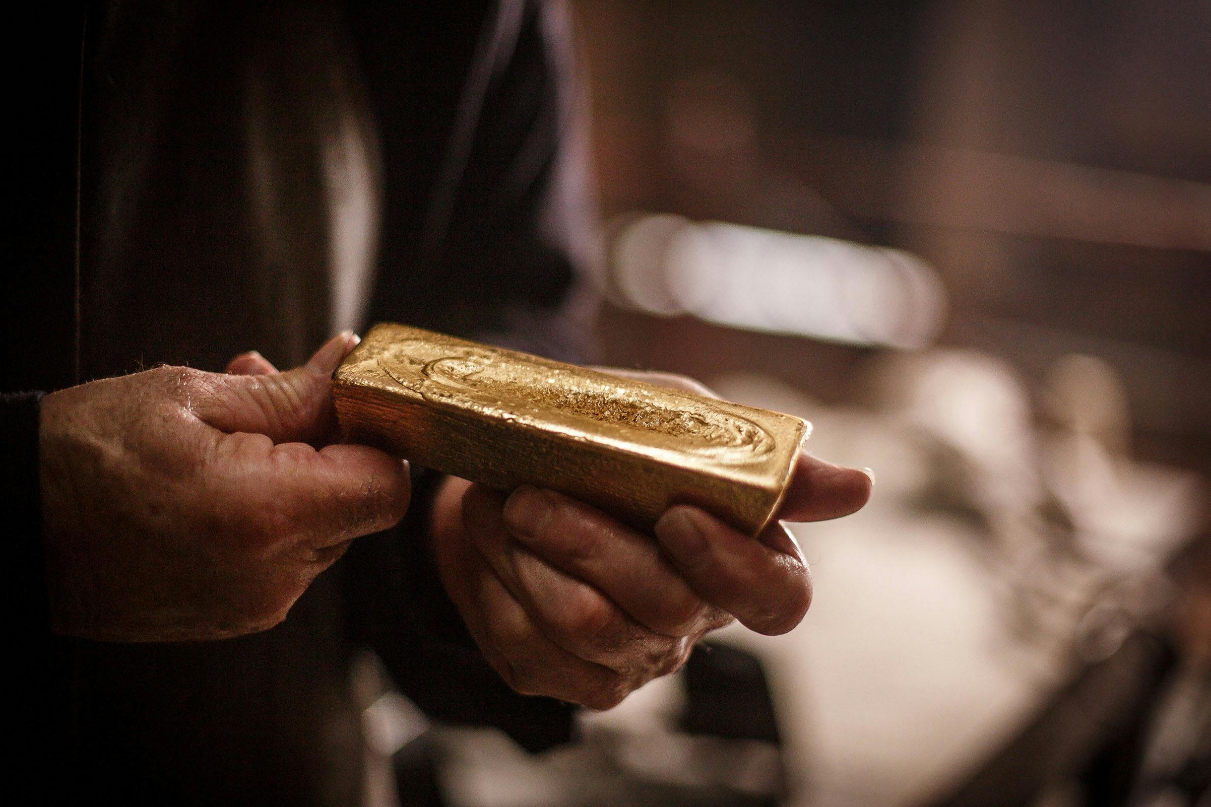 Close-up of hands holding a gold bar in a dimly lit setting.