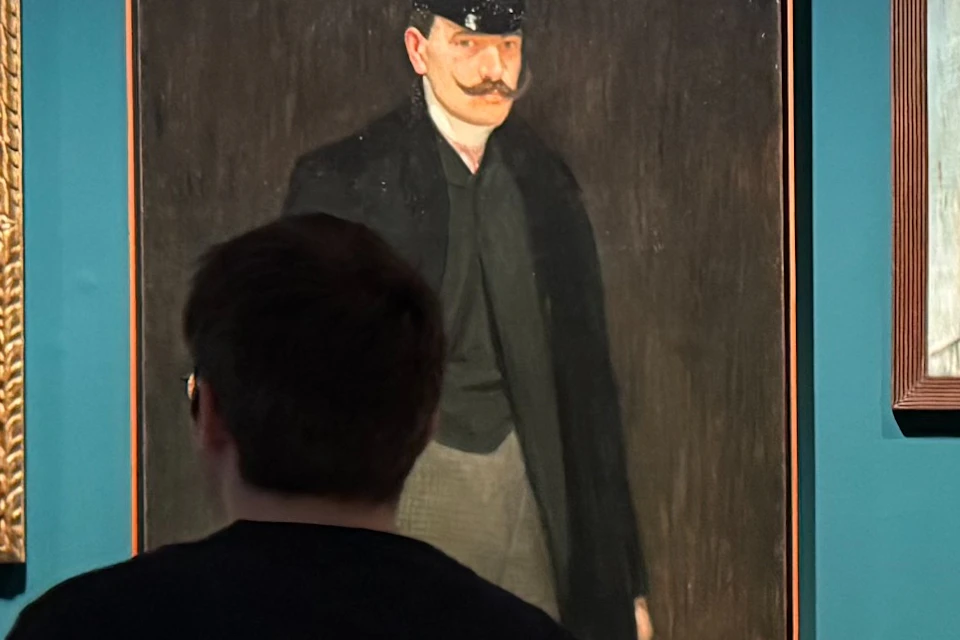 A dimly lit gallery with deep teal walls showcases a collection of Picasso’s early portraits.