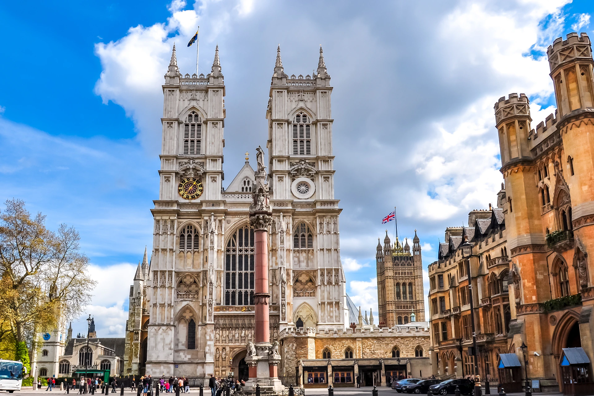 A view of Westminster Abbey with its twin towers, a statue in front, and the surrounding area under a partly cloudy sky.