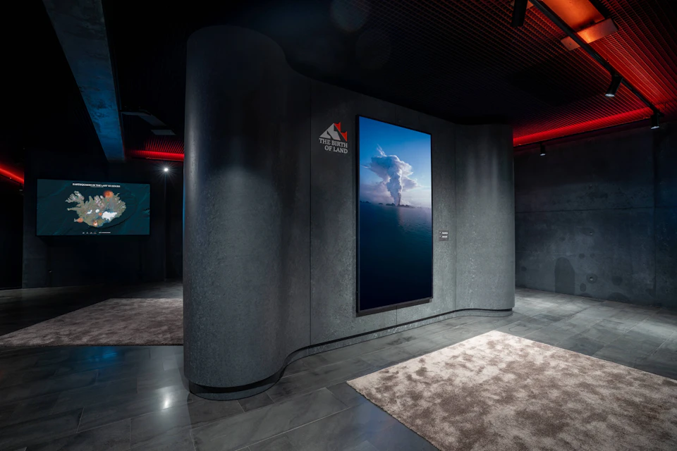 A modern interior with curved walls, a large screen displaying a volcano eruption, and a carpeted floor.