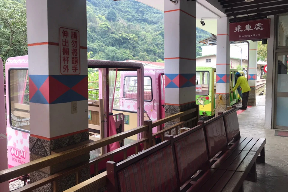 A train station platform with colorful train cars, wooden benches, and a sign with Chinese characters on a post.