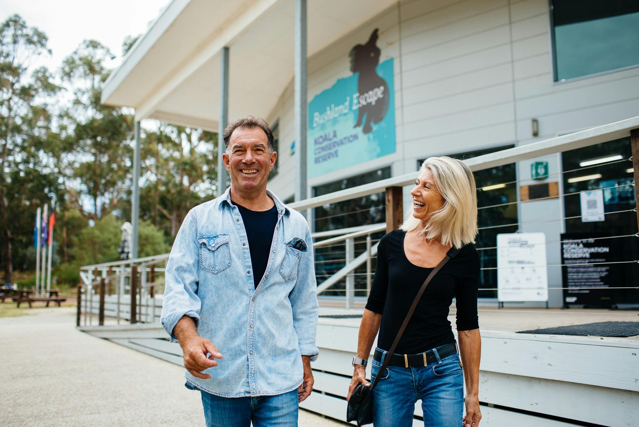 A man and a woman are smiling and walking outside a building with a visible sign for a koala conservation reserve.