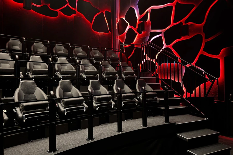 Empty cinema seating with luxurious black chairs and vibrant red and black geometric wall patterns. Elevated seating area.