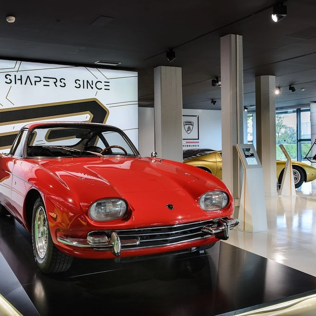 A red vintage car on display in a modern showroom with sleek lighting and signage in the background.
