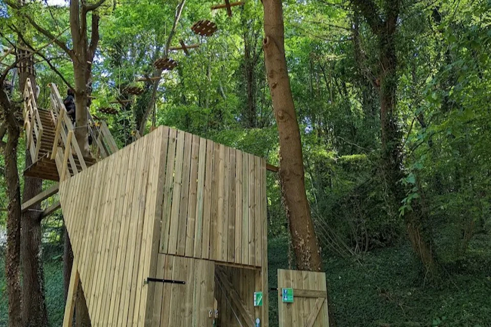 Wooden structures and climbing platforms in a lush green forest, with a rope adventure course among the trees.