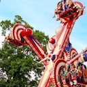 People enjoying a colorful amusement park ride with spinning seats, against a backdrop of trees and a blue sky.