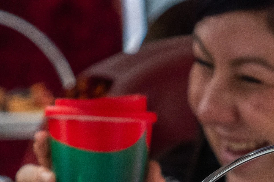 People enjoying an afternoon tea with tiered trays of cakes and sandwiches, holding festive red cups, smiling.