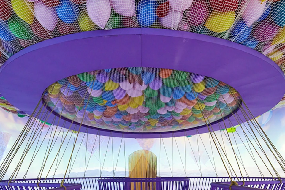 A colorful netted ceiling filled with balloons inside a purple structure, with a scenic view visible through its sides.