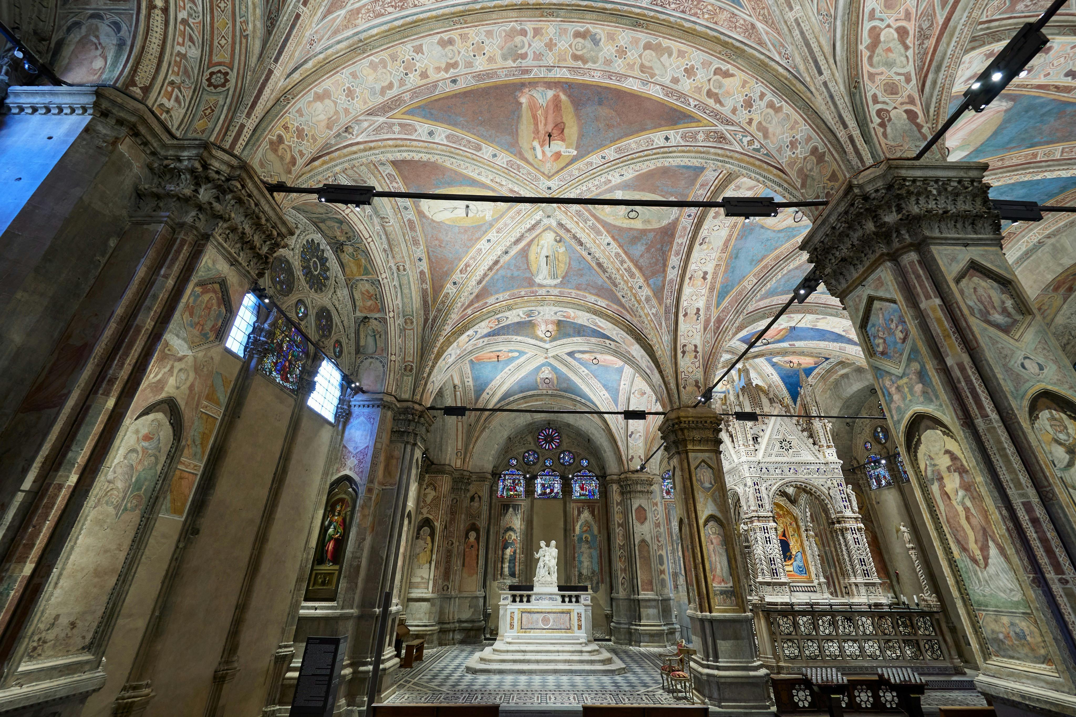 Ornate church interior with arched, frescoed ceilings, stained glass windows, and a central marble altar with a statue.