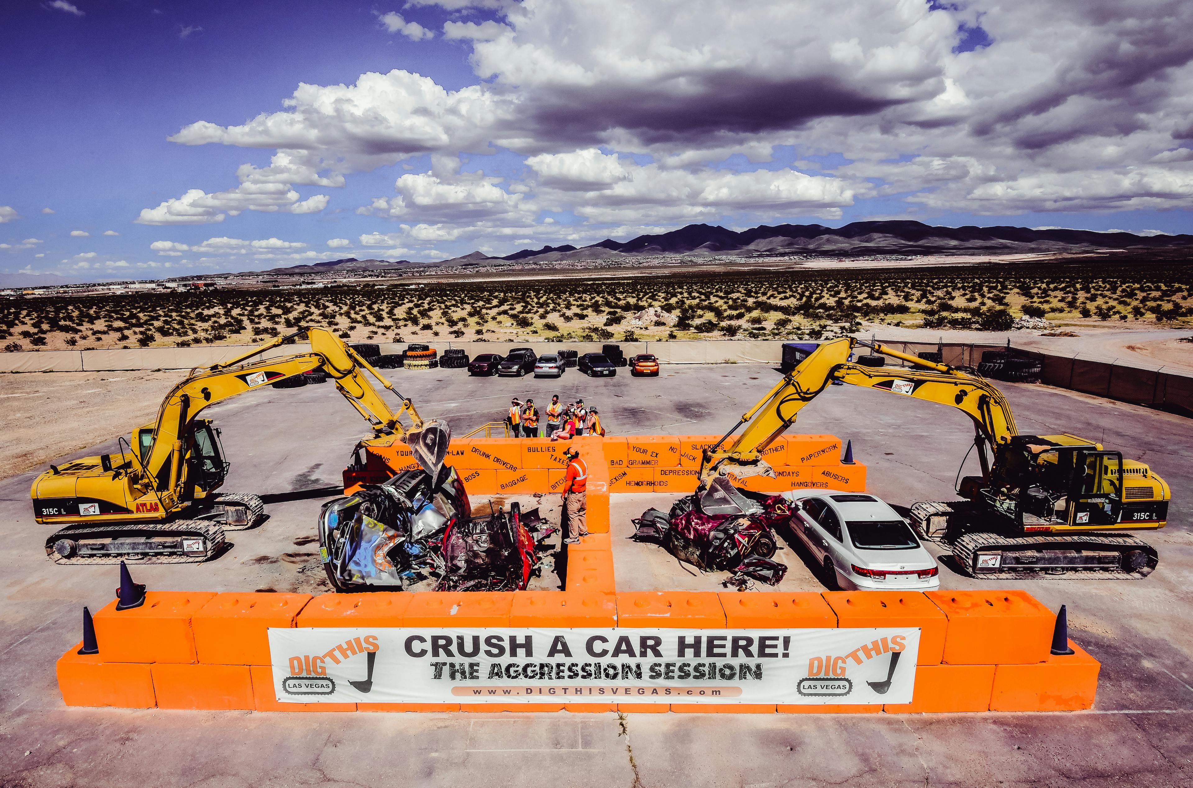 两台挖掘机在沙漠地带的橙色路障区域内粉碎汽车，标有“粉碎一辆汽车！” ，背景是山脉。