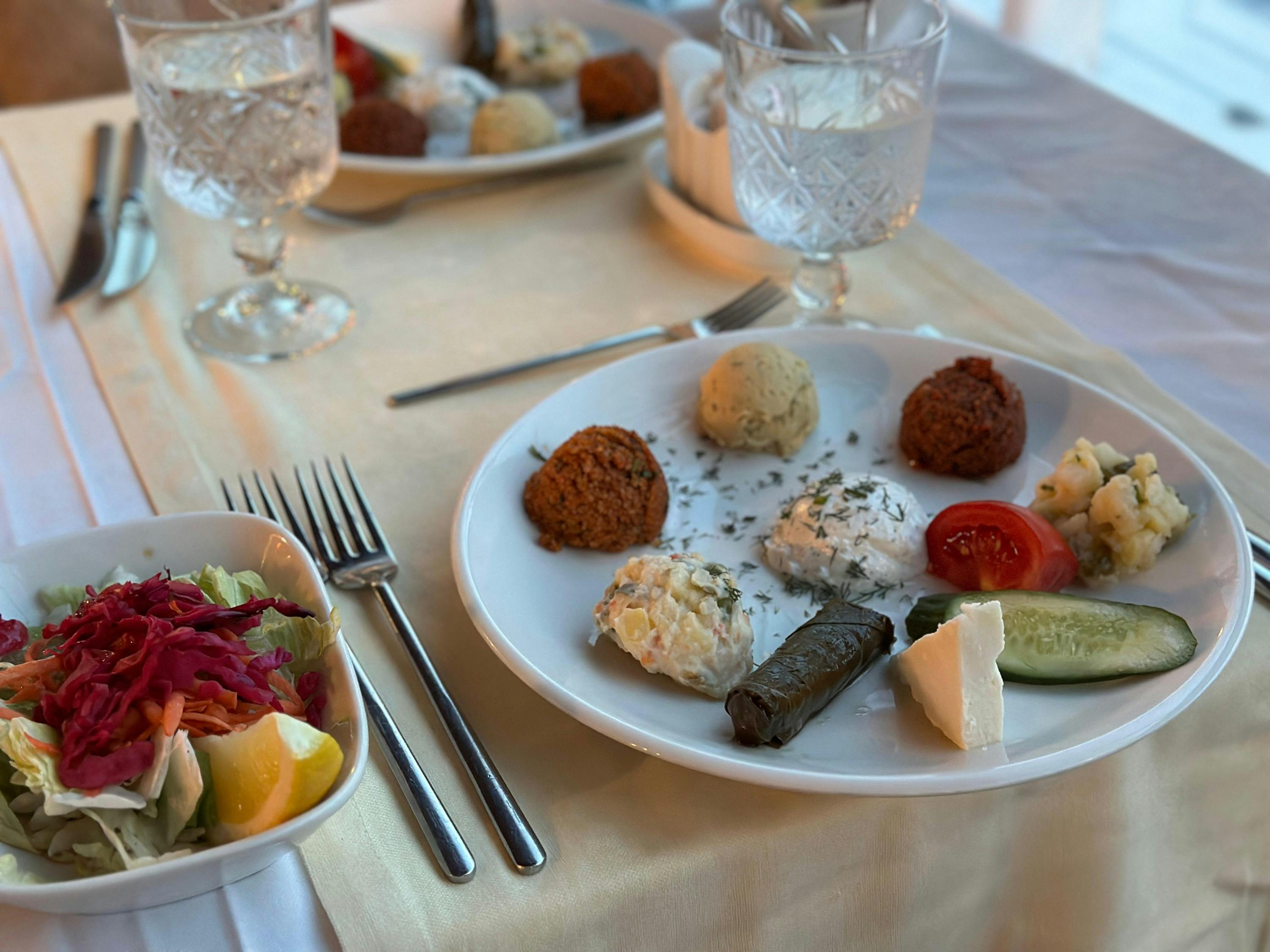 A plate with a variety of appetizers, including falafel, dolma, and salads, on a table set with glasses and cutlery.