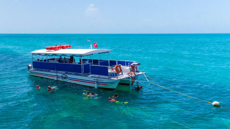 A catamaran with the name "Fury" on the side, anchored in clear blue water, with people snorkeling nearby.