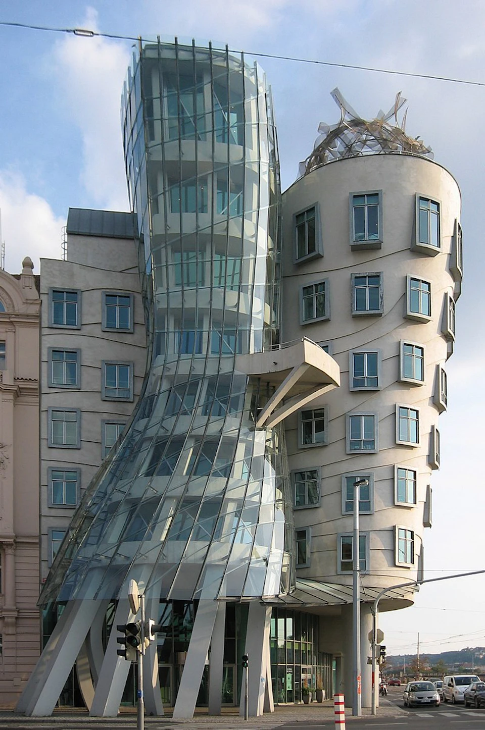 Modern building with a glass facade on the left curving into a beige stone structure with multiple windows on the right.