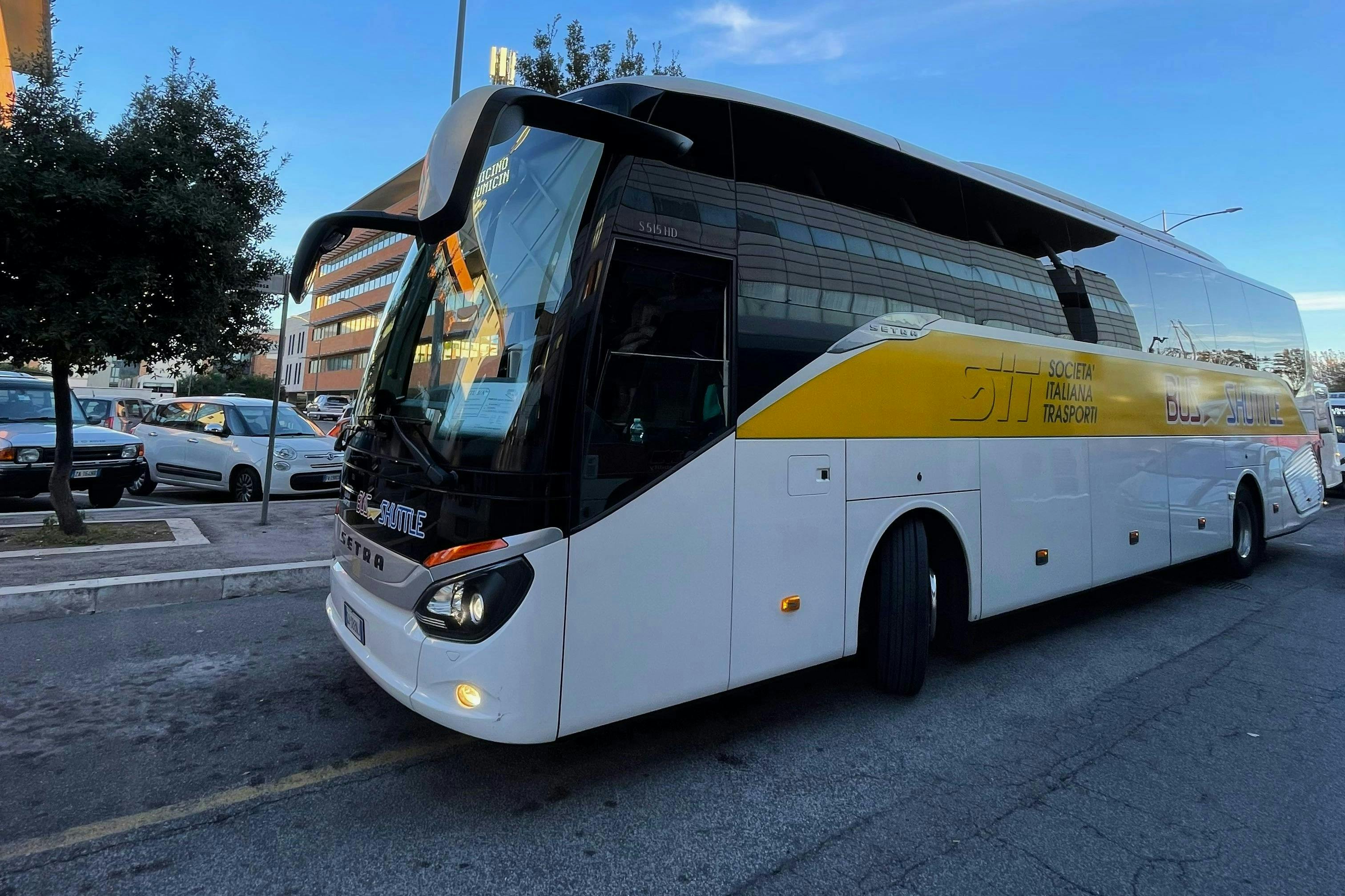 Ένα λευκό και κίτρινο πούλμαν με την ένδειξη "Societa Italiana Trasporti" σταθμευμένο σε έναν δρόμο της πόλης.