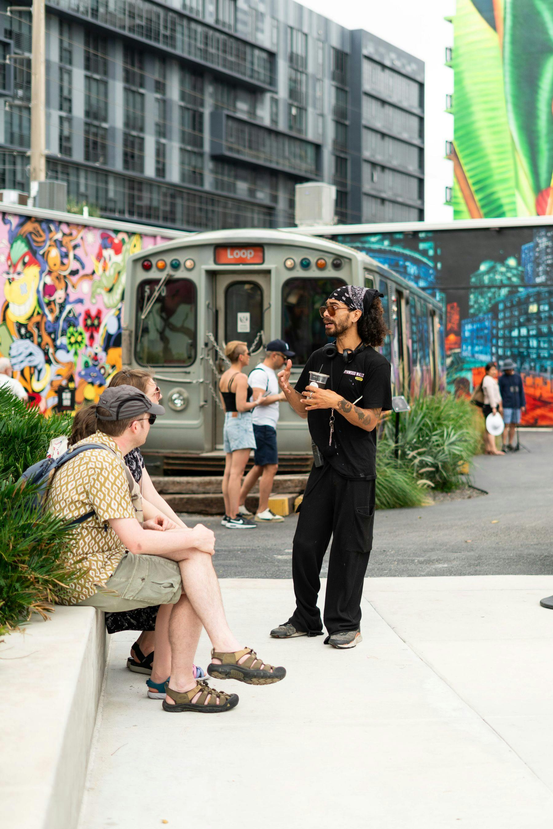 一名男子在充满活力、涂鸦覆盖的火车车厢和壁画前与一群坐着的人交谈。