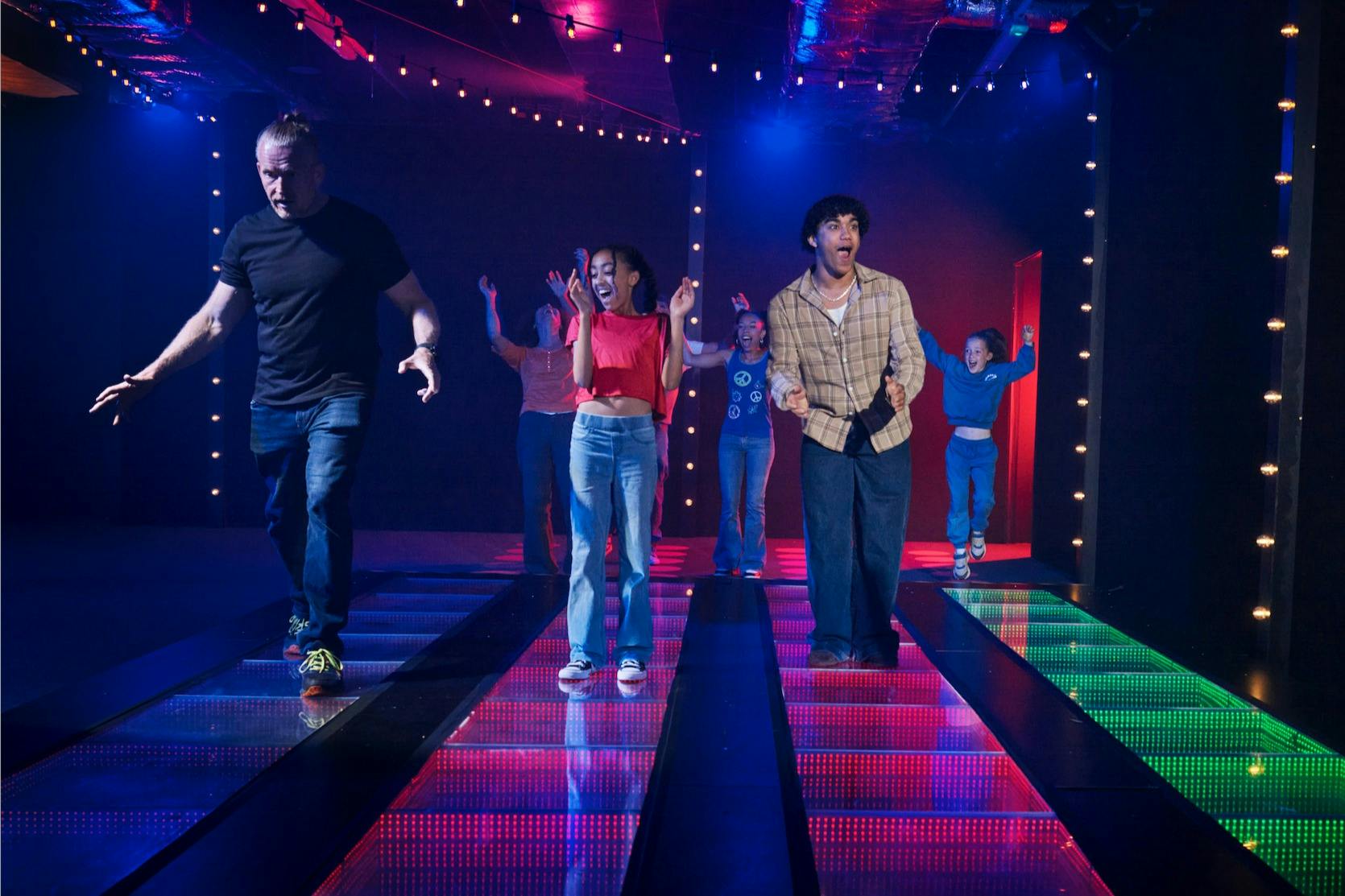 人们在色彩缤纷、灯火通明的地板上精力充沛地跳舞，地板上有弦灯和昏暗的背景。