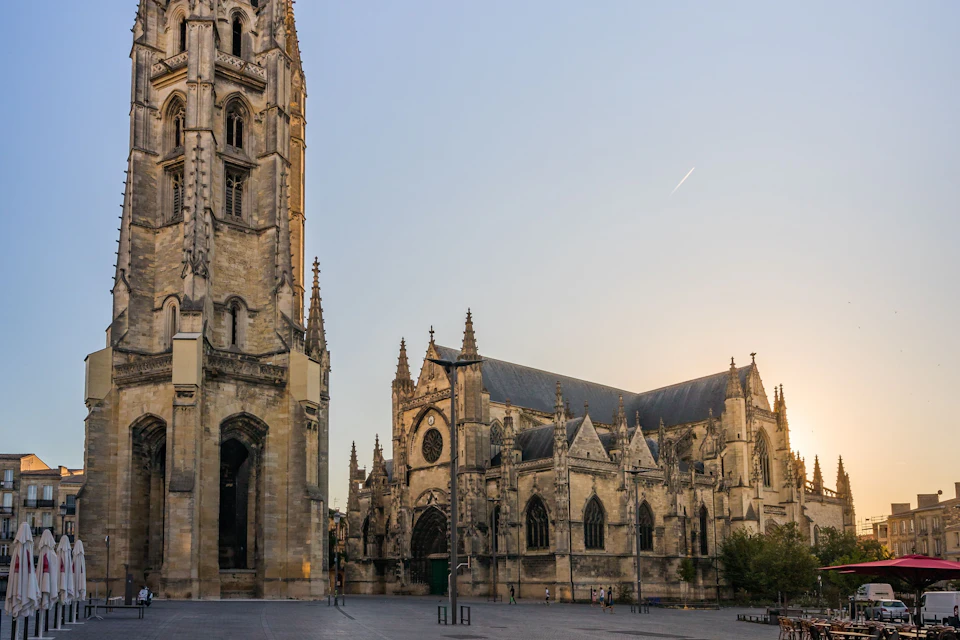 A gothic-style cathedral with a tall tower and intricate stonework is seen under a clear evening sky.