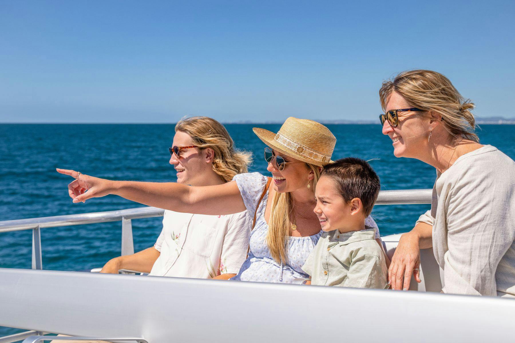 ボートに乗っている3人の女性と1人の男の子が、何かを指差しながら微笑んでいる。 澄んだ青い海が背後にあるサングラスと夏の服を着ています。