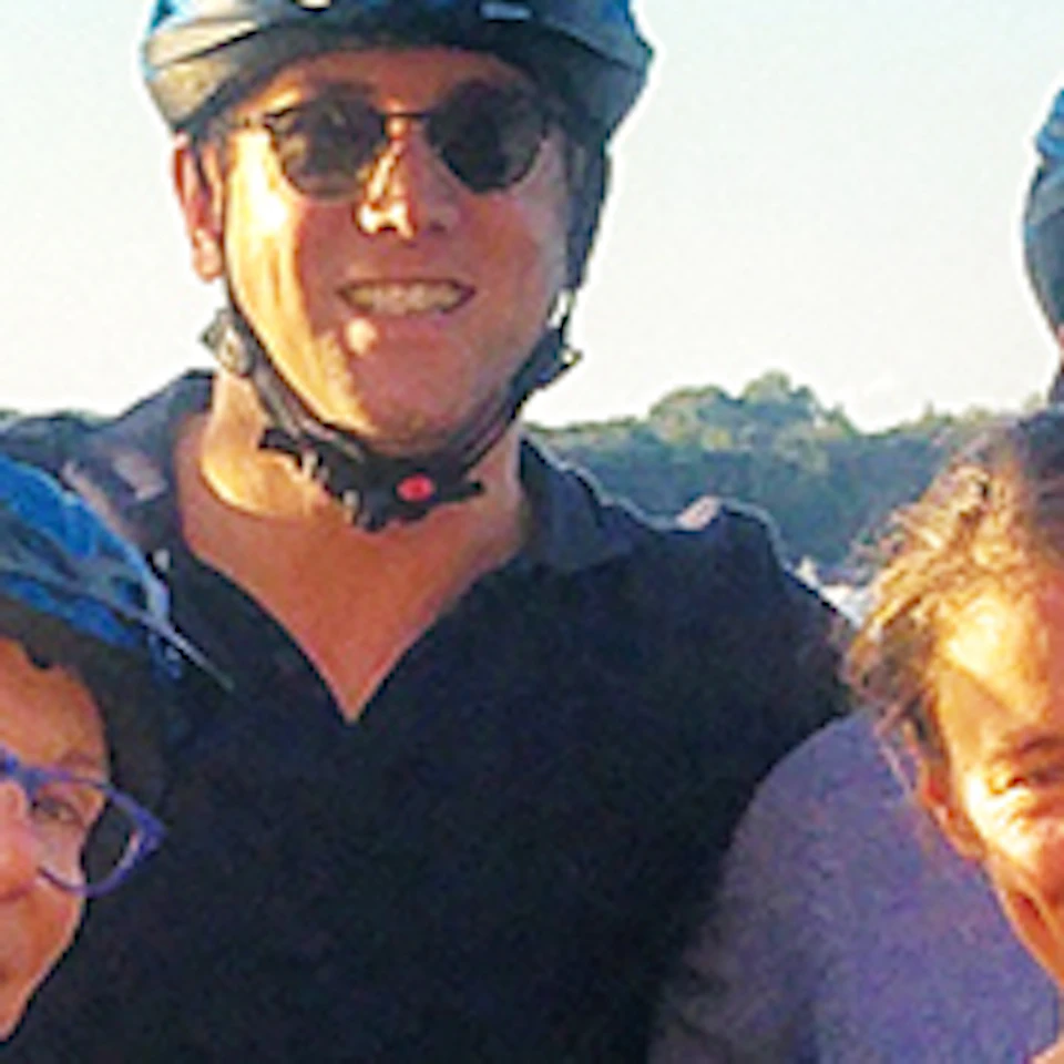 A group of people in helmets standing with bicycles in front of a historic building and wooden bridge over water.