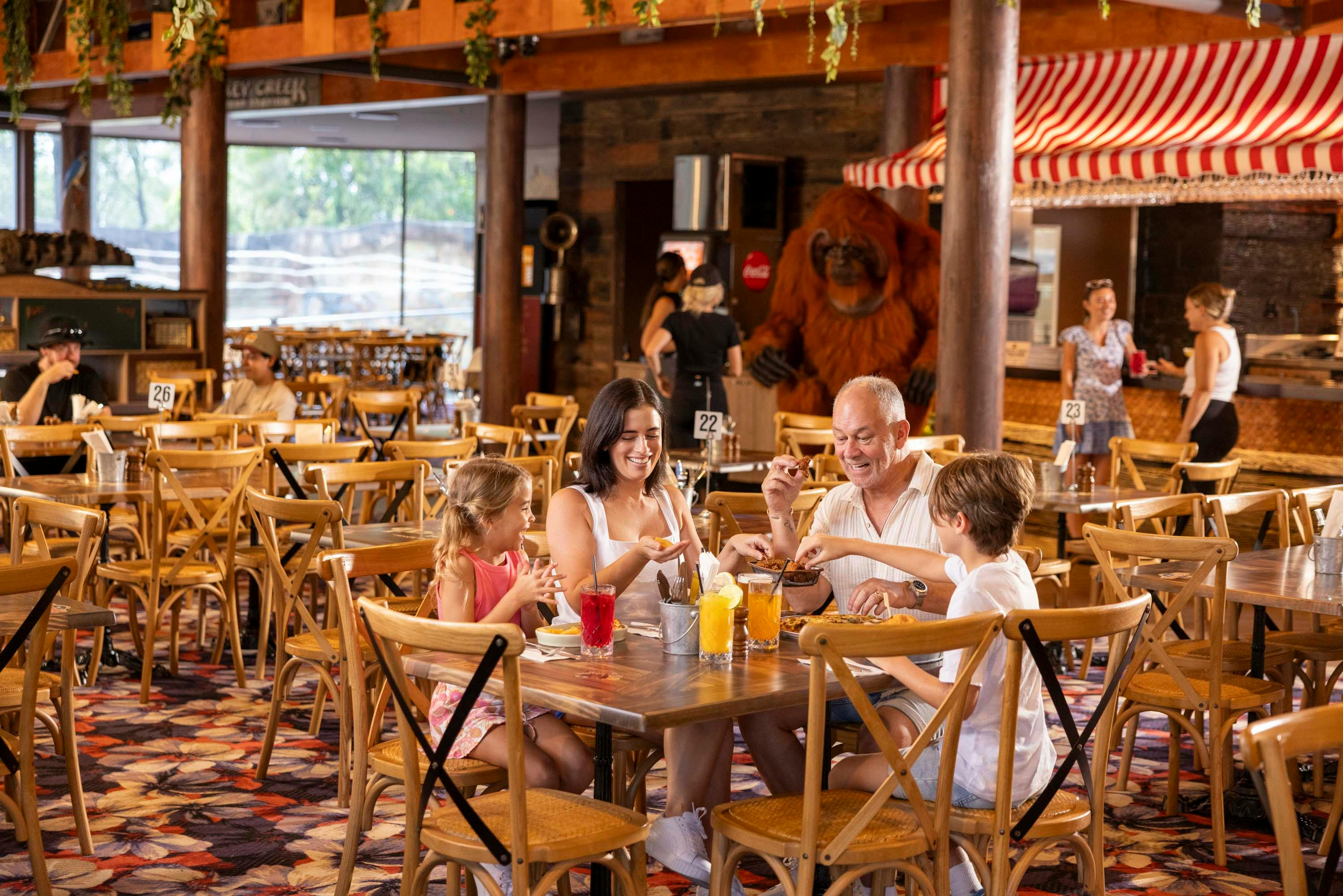 A family of four enjoys drinks at a restaurant with wooden decor and a jungle-themed atmosphere.