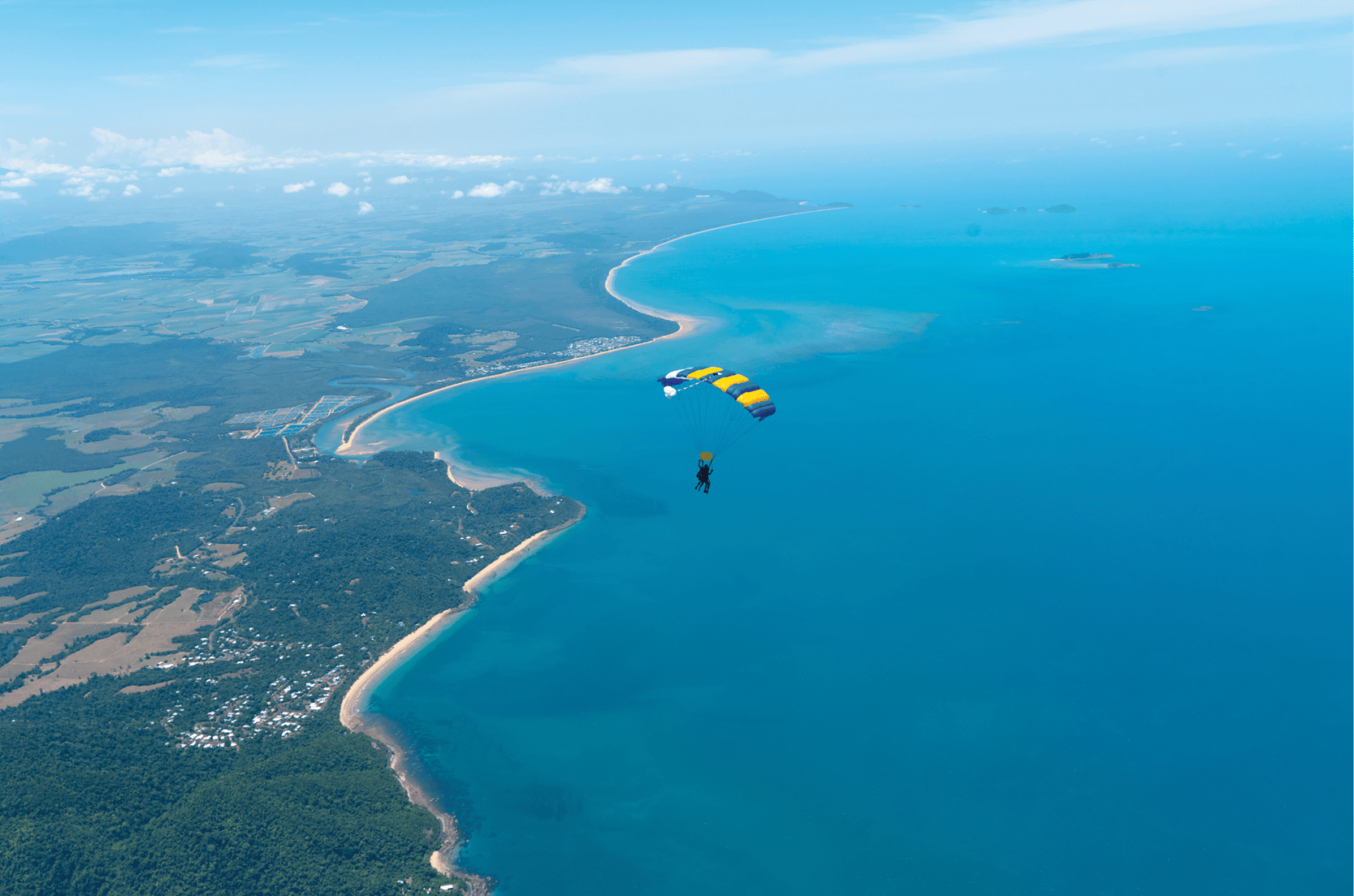 一个人在晴朗的天空下跳伞，俯瞰郁郁葱葱的绿色和蓝色的海水。