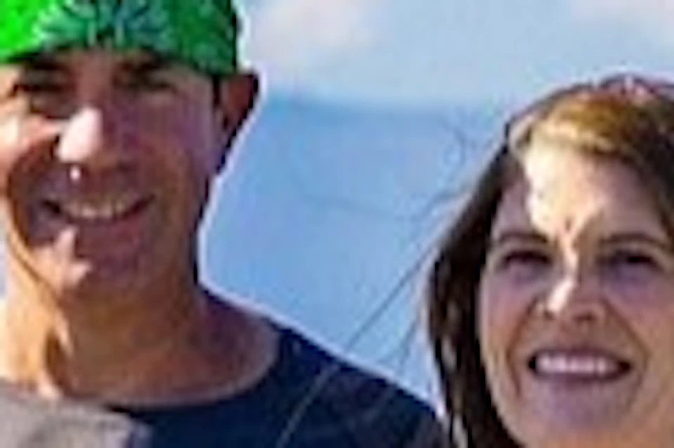 Two people in athletic wear stand smiling next to a row of bikes with a scenic mountain backdrop.