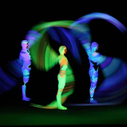 Tre figurer i glödande neonfärger rör sig mot en svart bakgrund och skapar levande ljusspår och dynamiska mönster.