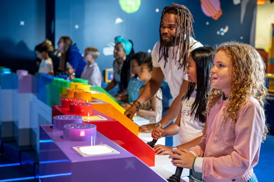 Children and an adult engage with colorful interactive exhibits, set against a wall decorated with space-themed elements.