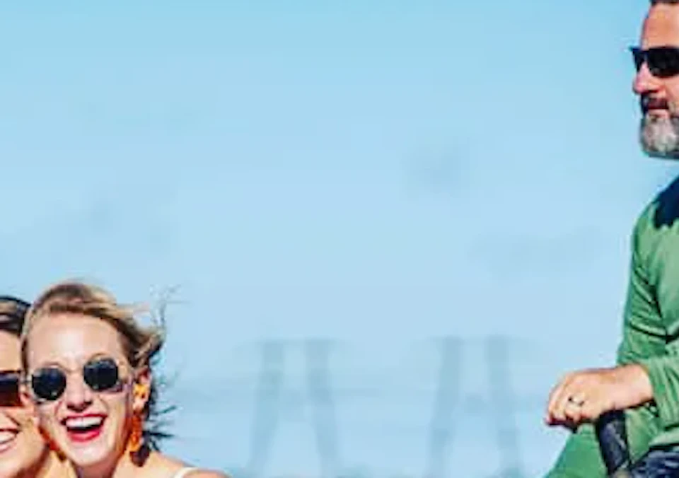 Two women and a man ride on an airboat through a grassy wetlands area under a clear blue sky.