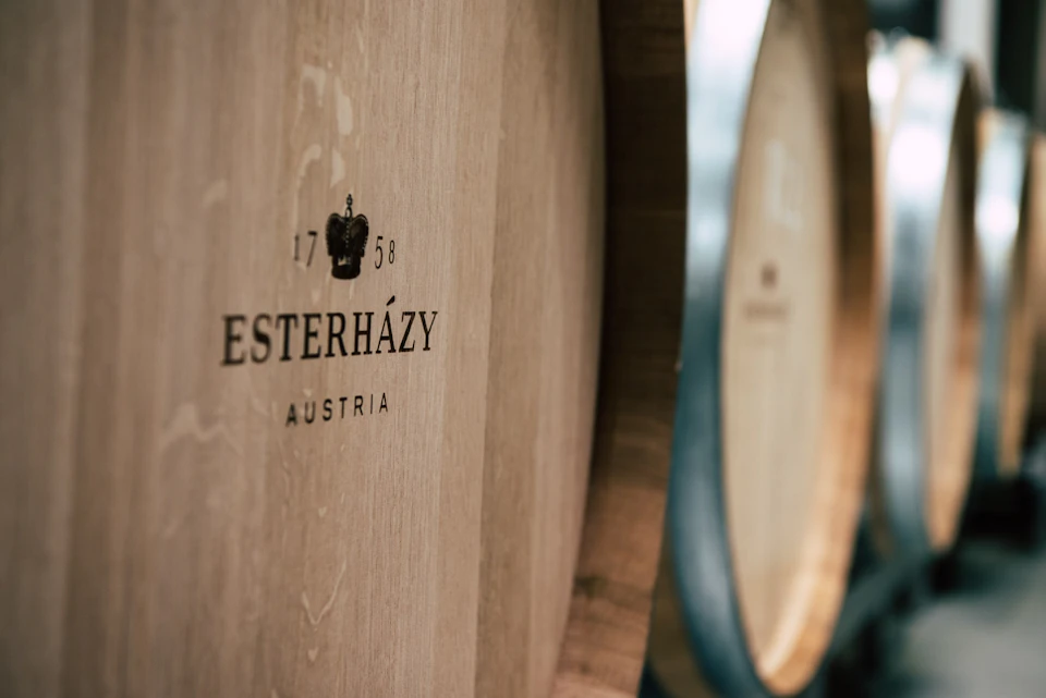 Close-up of wooden barrels with "Esterházy Austria" and "1758" printed on one. Details of the other barrels are out of focus.