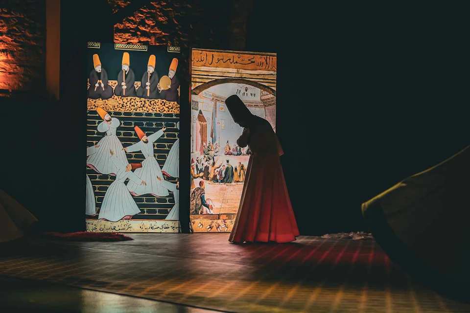 A person in a traditional outfit performing in front of illuminated panels with artistic and calligraphic designs on a stage.