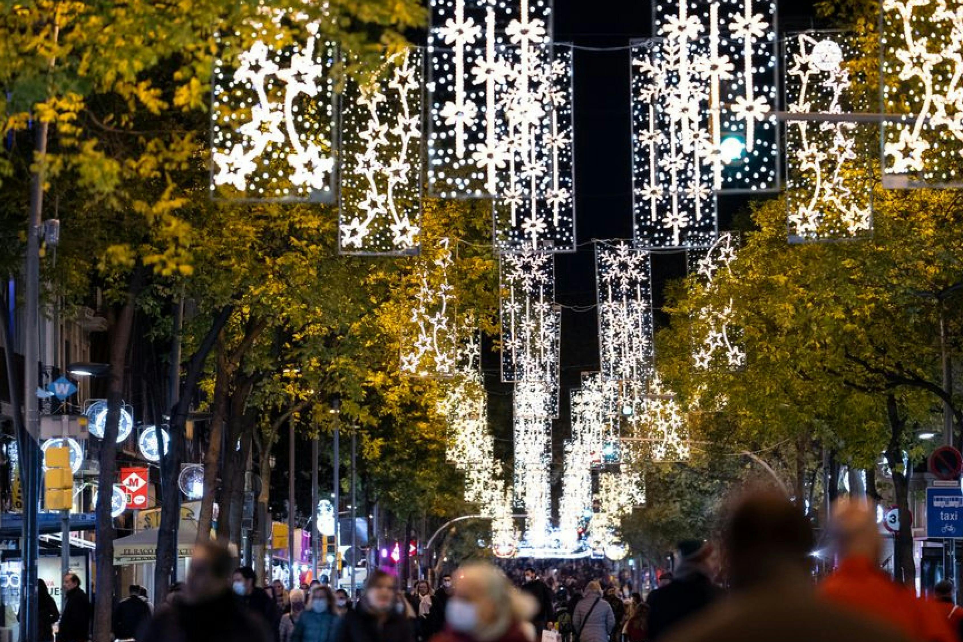 A street at night with hanging festive lights and illuminated decorations. People are walking beneath the lights.