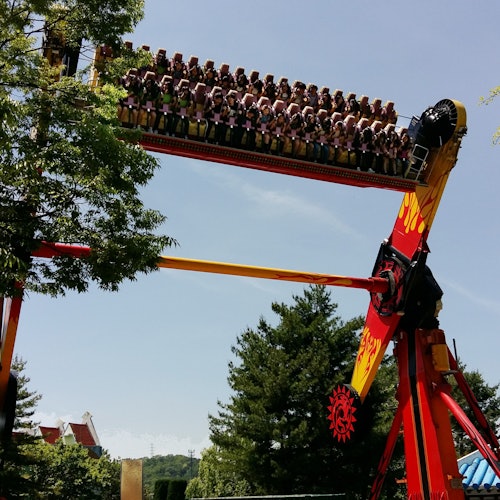 People seated on a swinging amusement park ride, elevated upside down against a backdrop of trees and a clear sky.