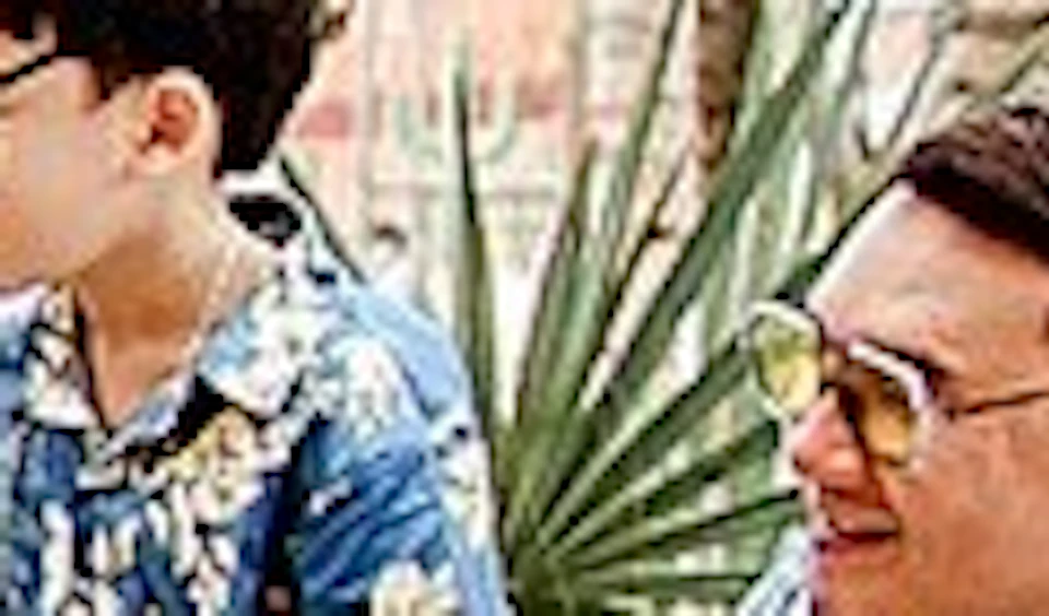 Three people in blue-patterned outfits stand by a wooden fence in a zoo-like setting with plants and enclosures.