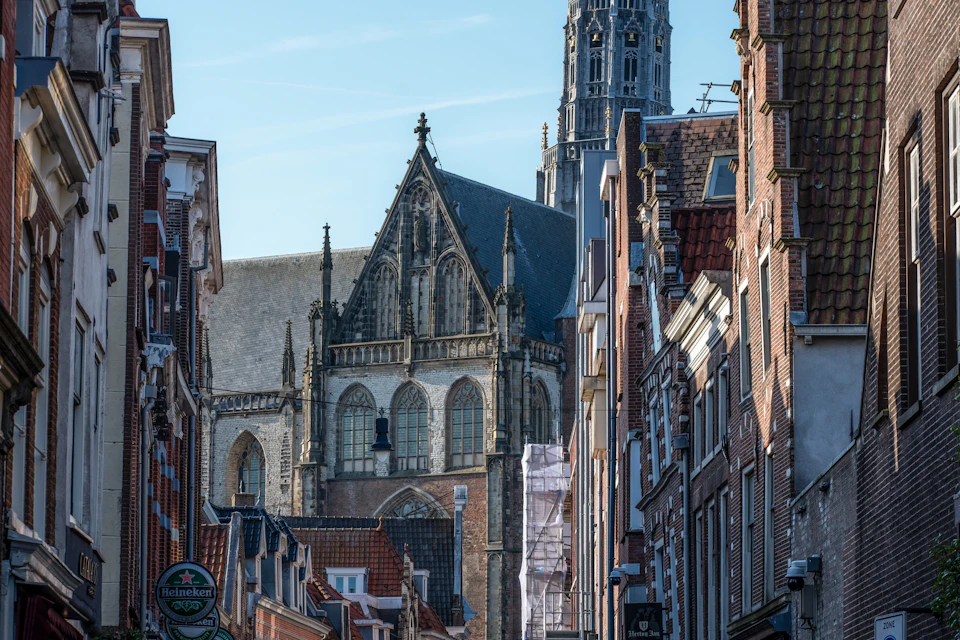 A view of a historic church with a pointed roof and tall tower, surrounded by brick buildings under a clear sky.