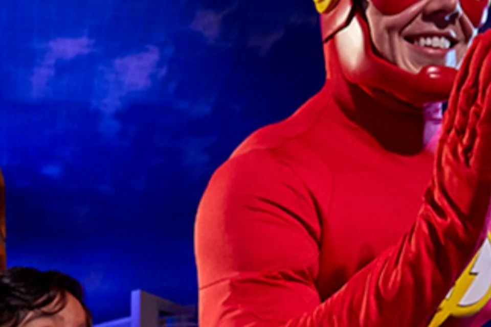 A child wearing a Flash-themed shirt poses joyfully next to a person in a Flash superhero costume in an urban evening setting.