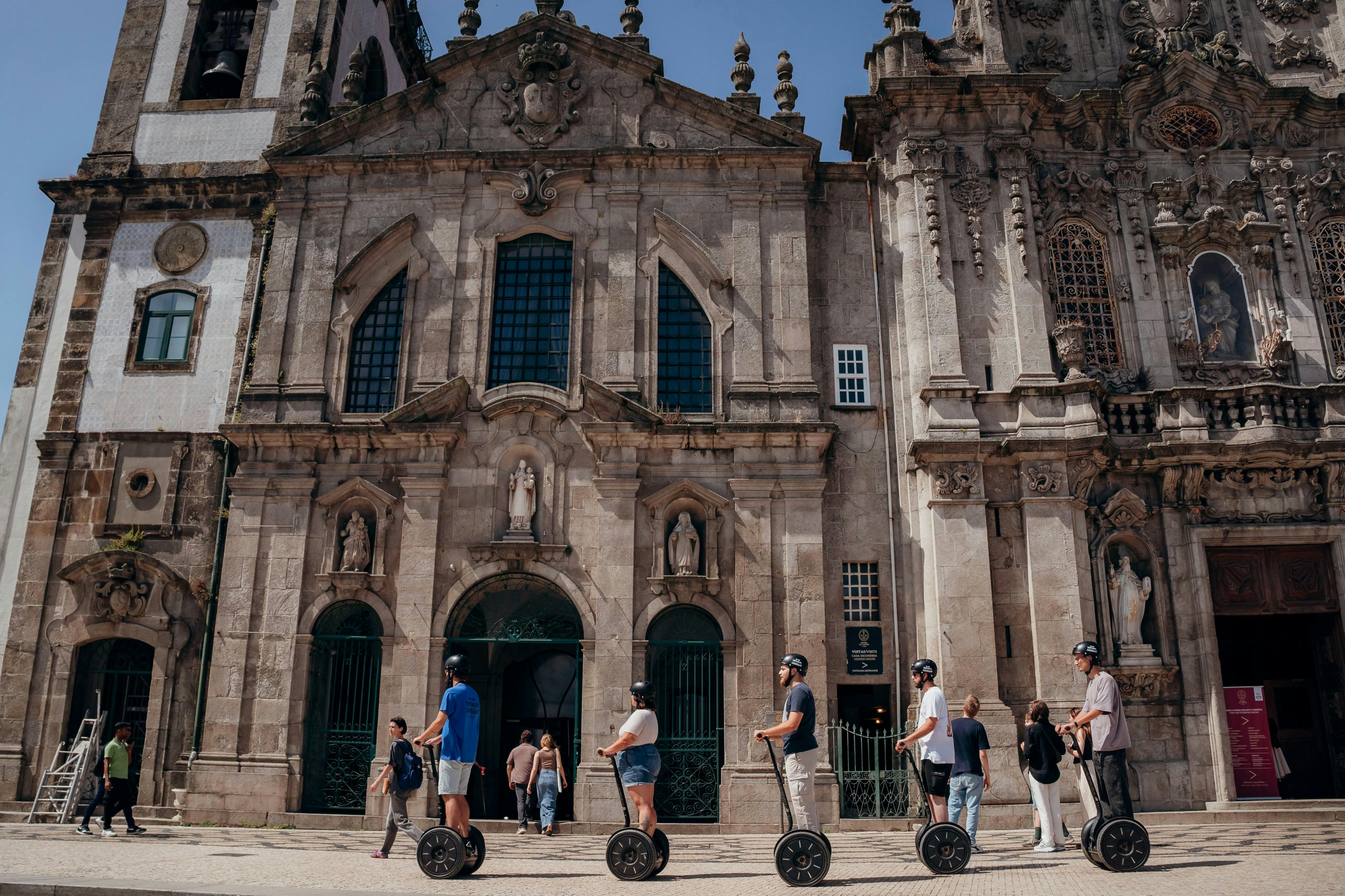아치형 창문과 조각상이 있는 유서 깊은 석조 건물 앞에 세그웨이를 타고 있는 5명의 사람들. 근처에 다른 보행자가 있습니다.