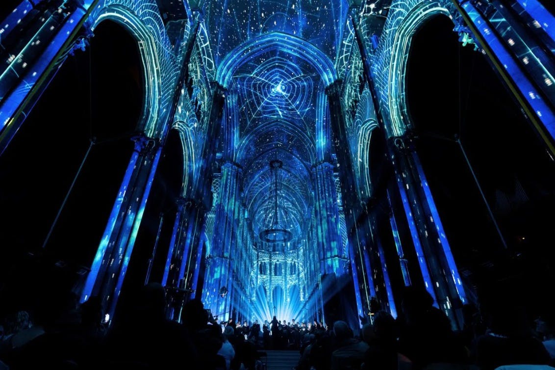 Um interior de catedral iluminado com projecções de luz azul, com padrões intrincados nos arcos e no teto.