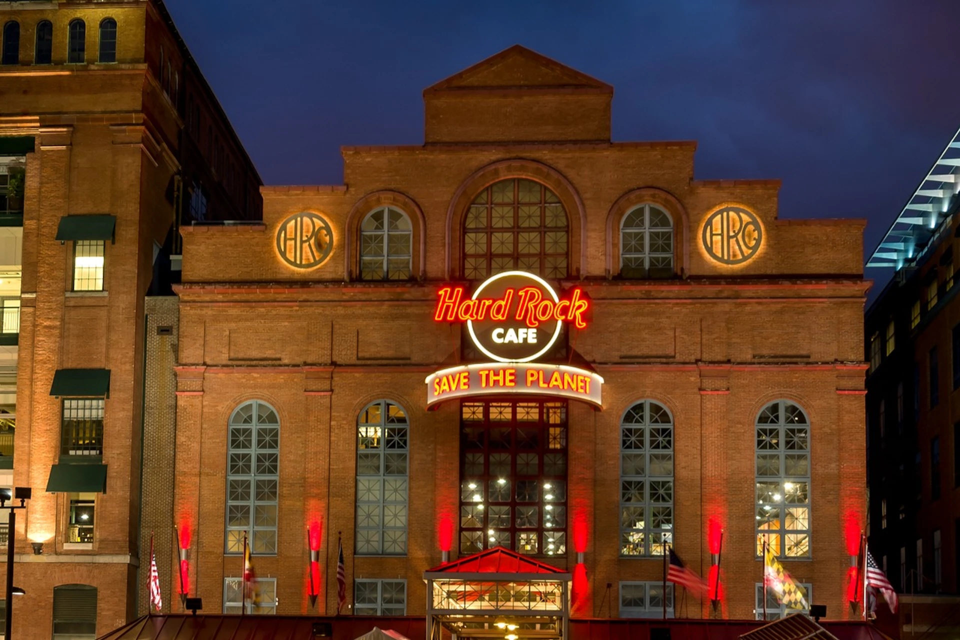 Brick building with large windows, neon signs reading "Hard Rock Cafe" and "Save The Planet," illuminated by red lights at night.