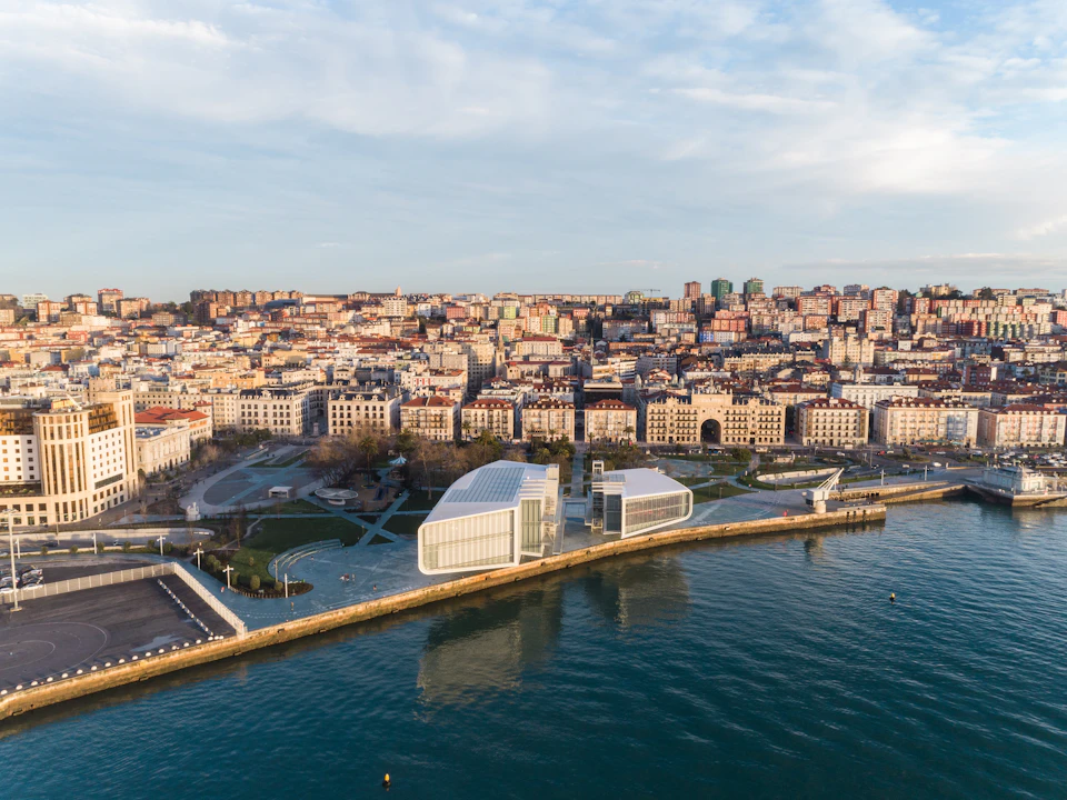 Aerial view of a coastal city with modern white buildings along a waterfront, dense urban area, and clear water.