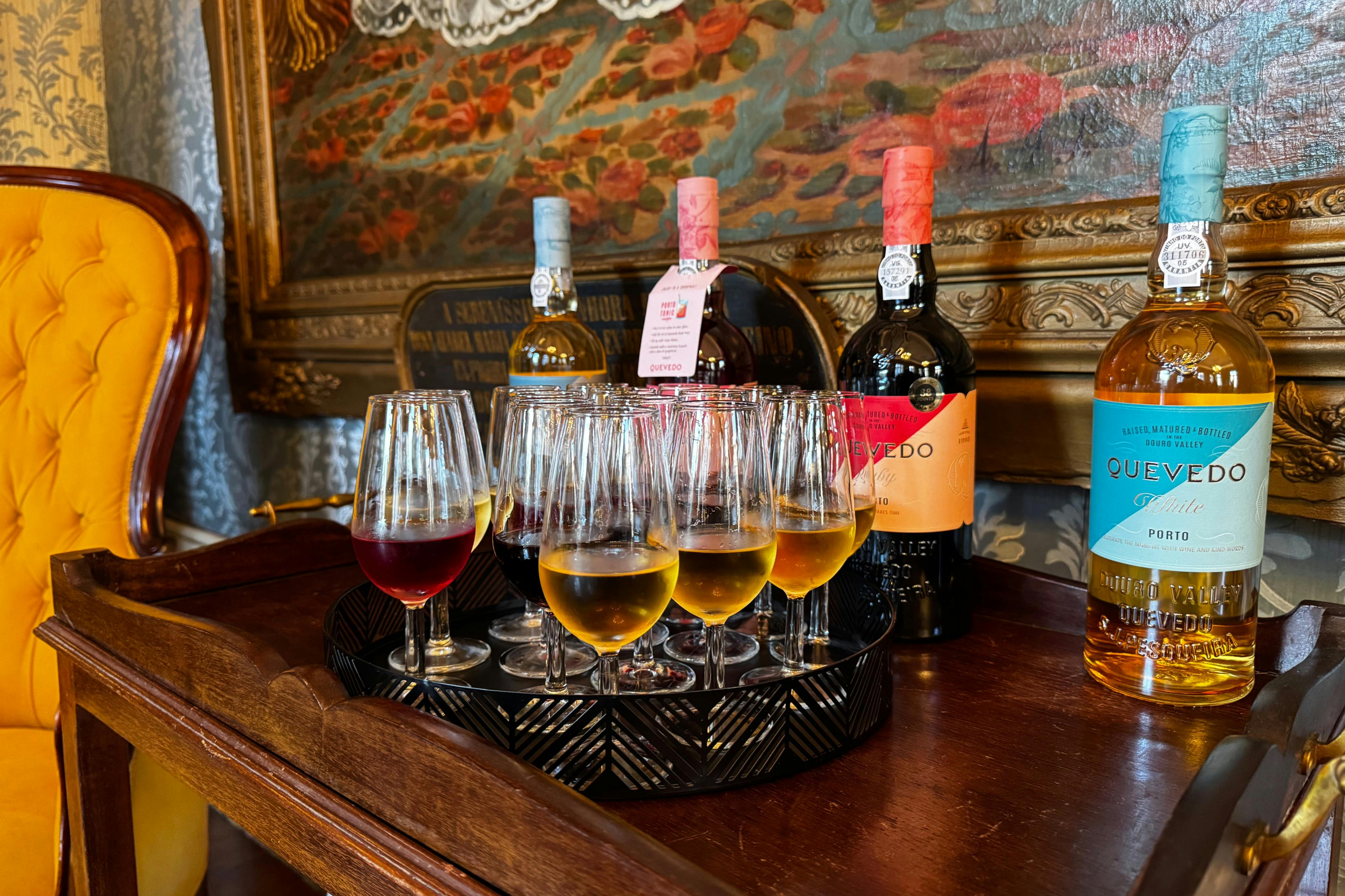 A tray with several wine glasses filled with different colored wines, with bottles of wine and a decorative painting behind.