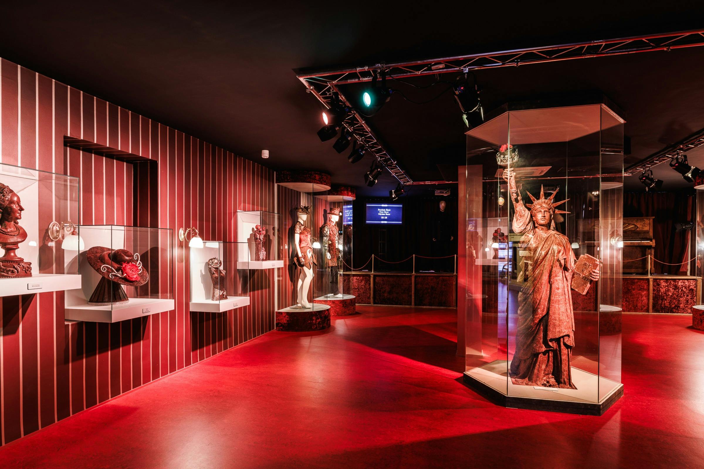 Une exposition dans un musée avec des costumes, des accessoires et une statue de la liberté dans une pièce faiblement éclairée avec un sol rouge.