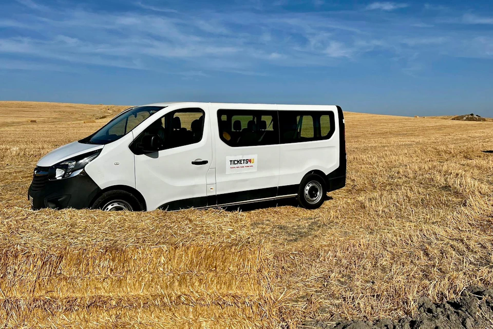 A white van with a company logo is parked in a dry, harvested field under a blue sky.