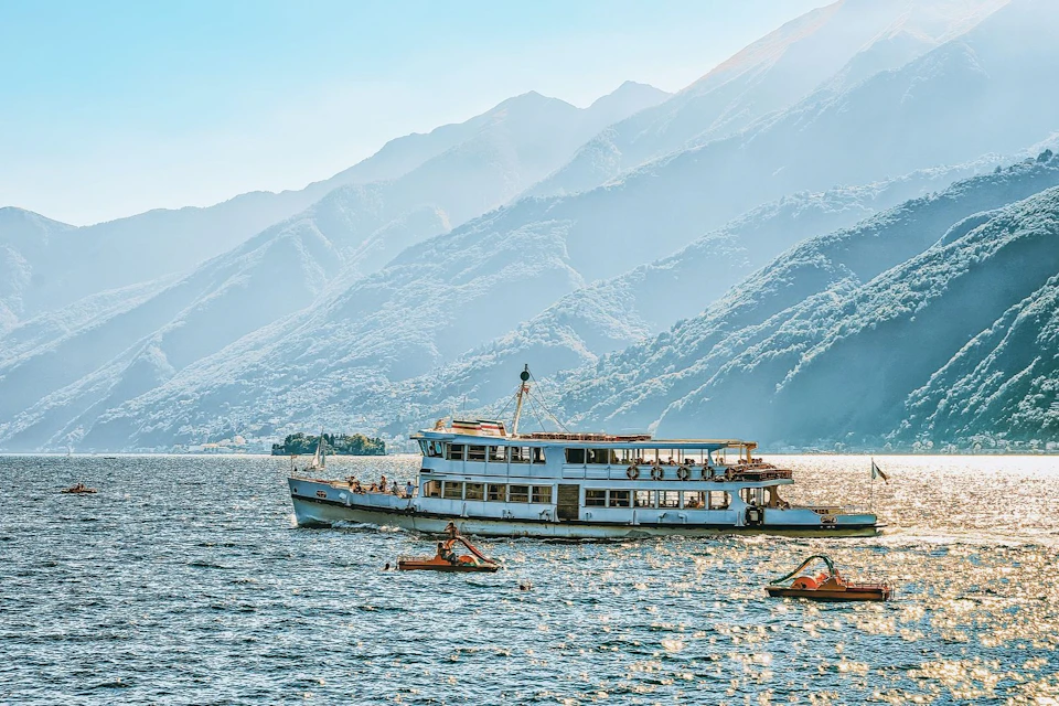 A boat on a scenic lake with people enjoying activities, surrounded by mountains under a clear sky.
