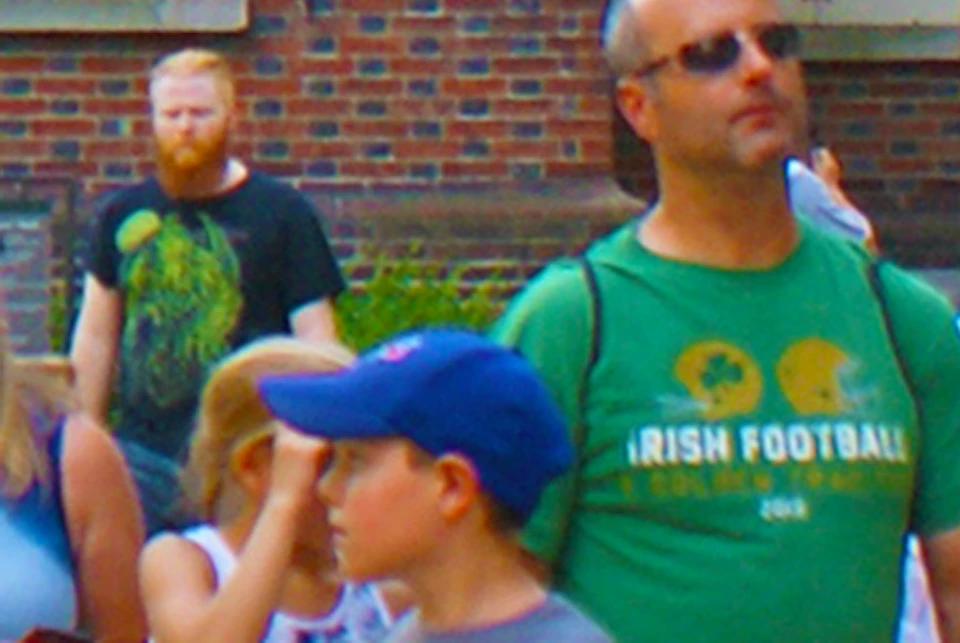 A group of people, including children, walk and explore near historic brick buildings with arched windows and white shutters.