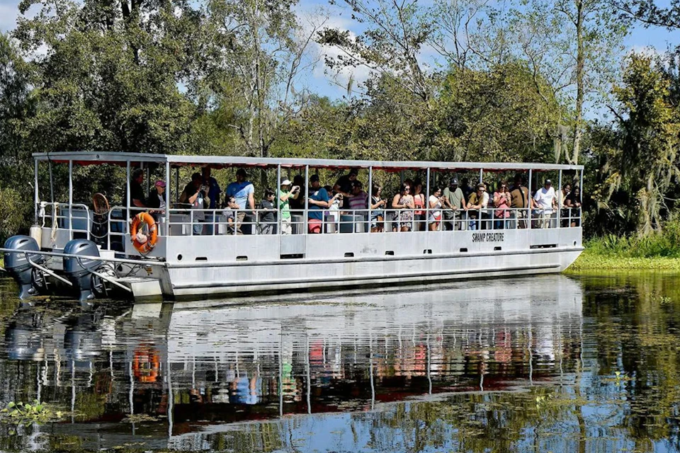 A boat with a group of people on board cruising through a calm waterway surrounded by trees and foliage.